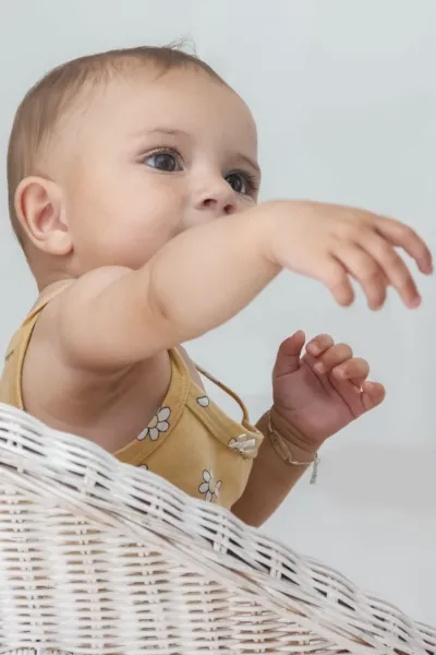 lekarz od skóry dla dzieci w Lublinie, słodkie niemowlę w żółtym śpioszku w białe kwiatki, sięgające po coś.