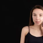 domowe sposoby na trądzik: Młoda kobieta z niedoskonałościami i kremem na policzku, delikatnie dotyka twarzy.